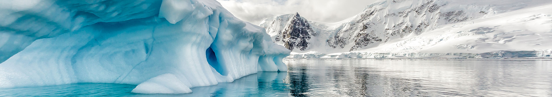 interesting blue iceberg formation in calm Antarctic waters in Polar Circle with snowy mountains in background